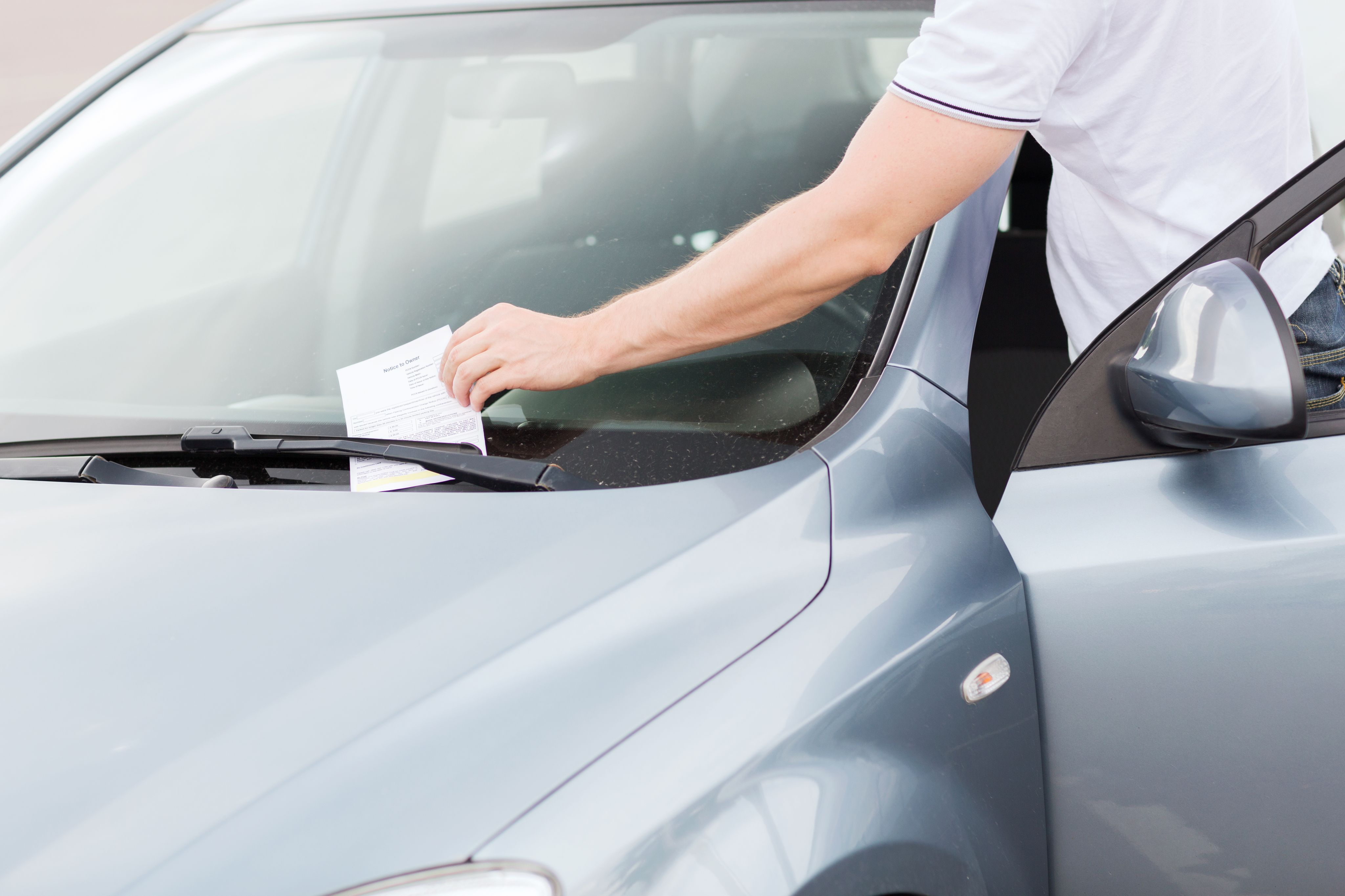 image of a man taking a parking violation of a car windshield